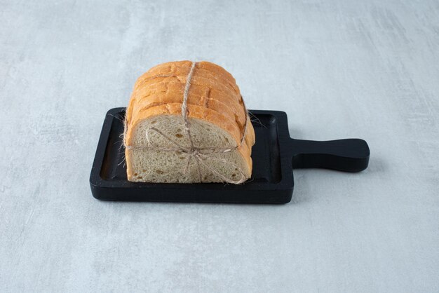 Белый хлеб, перевязанный веревкой на темной доске.