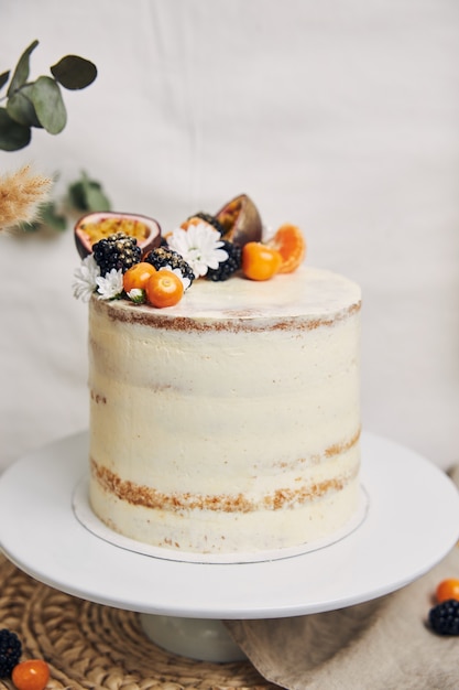 White cake with berries and passionfruits next to a plant behind a white background