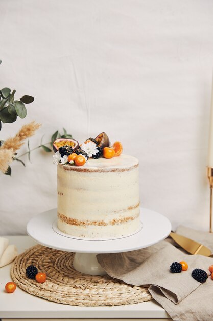 White cake with berries and passionfruits next to a plant behind a white background