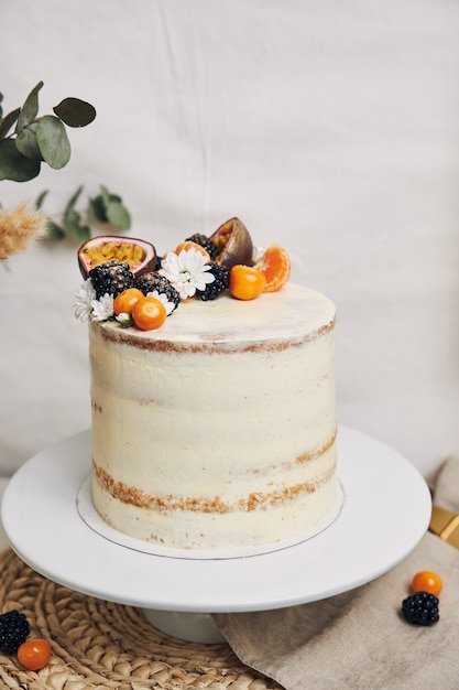 White cake with berries and passionfruits next to a plant behind a white