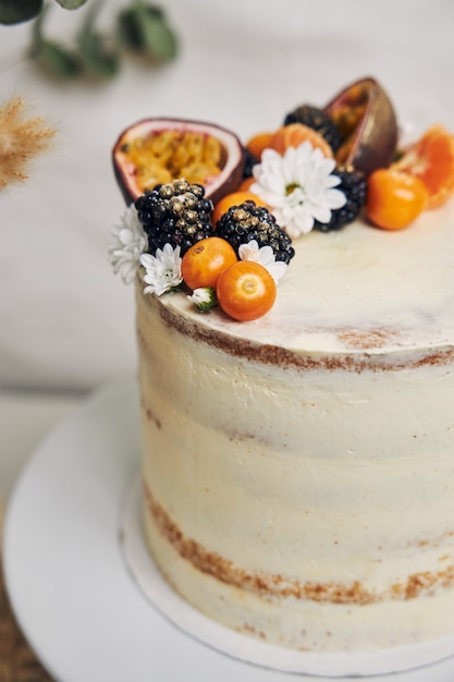 White cake with berries and passionfruits next to a plant behind on white
