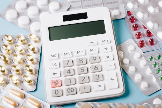 Белый калькулятор и таблетки на синем фоне как символ платной (дорогой) медицины