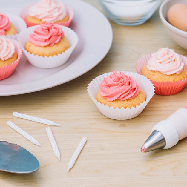 White candles; cupcake and icing bag on wooden desk