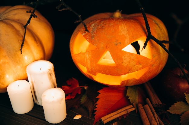 White candles stand before scarry Halloween pumpkin on cinnamon