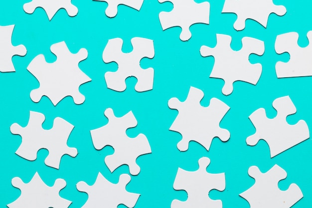 White cardboard jigsaw puzzles pieces on turquoise backdrop