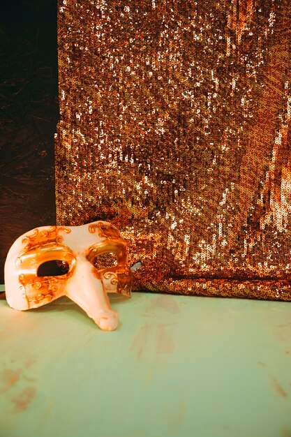White carnival mask near the glitter golden sequins textile on green weathered surface