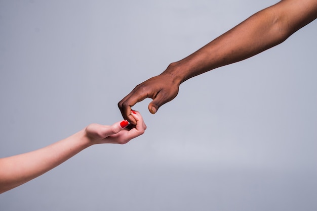 White caucasian female hand and black male hand holding fingers together