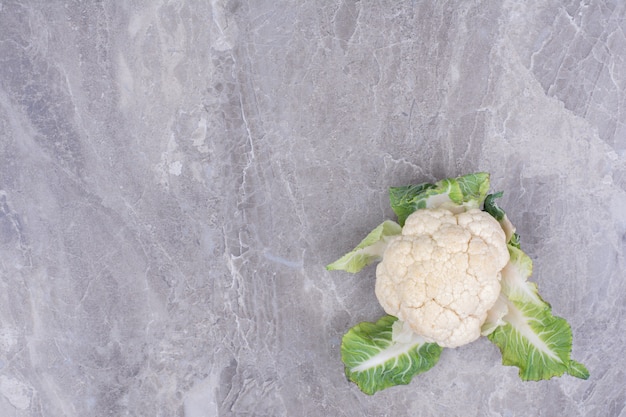 Cavolfiore bianco con foglie verdi su marmo.