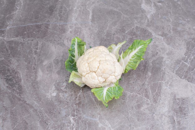 A white cauliflower with green leaves on the marble