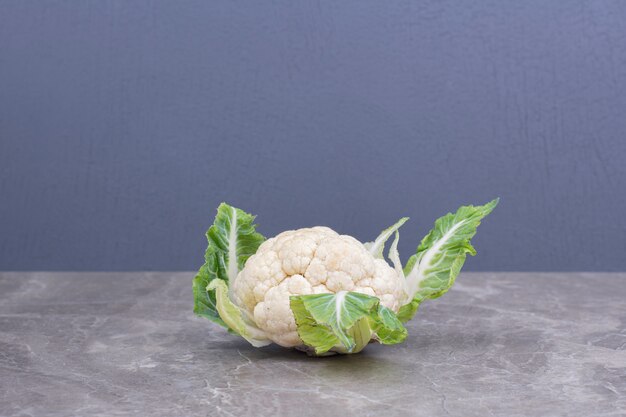 White cauliflower with green leaves on the marble