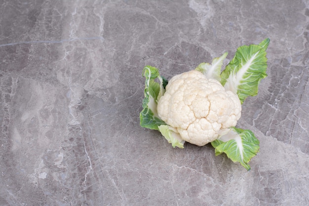 Free photo white cauliflower with leaves on a marble surface