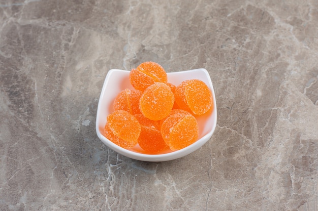회색 표면 위에 오렌지 젤리로 가득 찬 흰색 세라믹 그릇.
