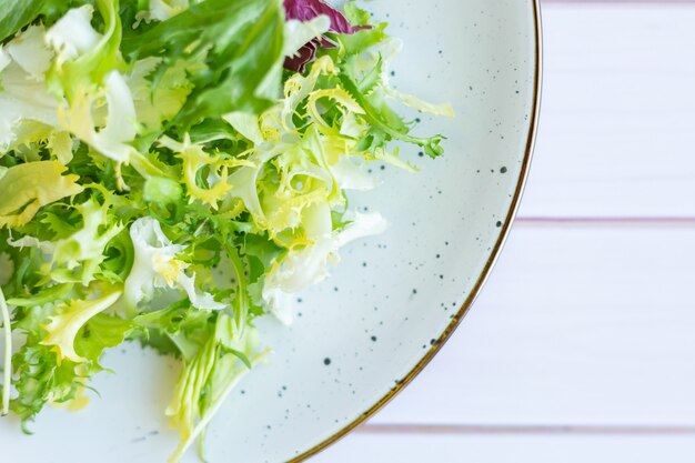 Белая керамическая тарелка со свежим салатом на деревянной поверхности