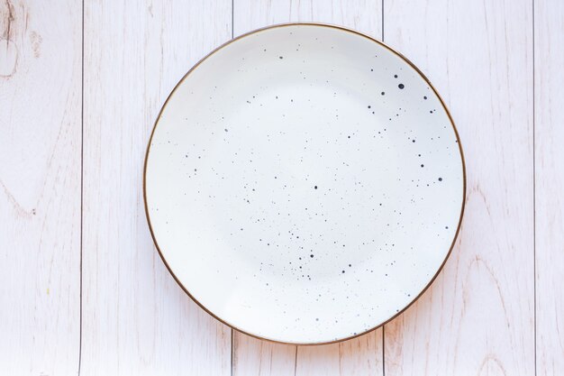 Белая керамическая тарелка на деревянной поверхности, вид сверху