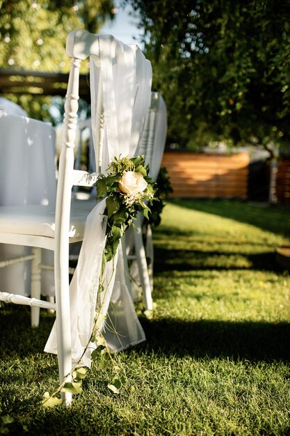 屋外の結婚式の会場でバラの花束と白い椅子。