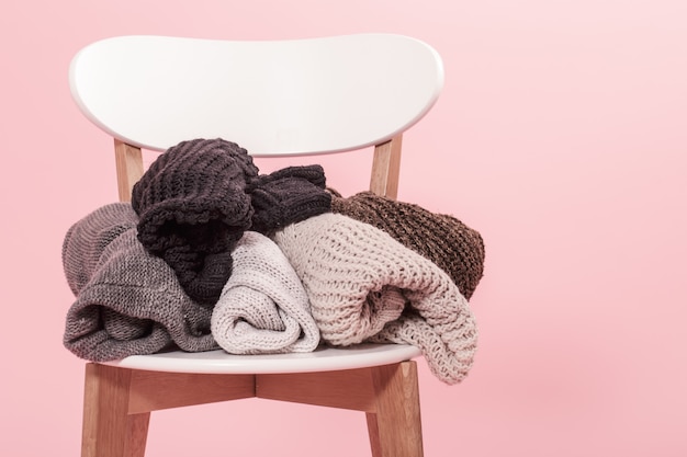 White chair with a stack of knitted sweaters on a pink background