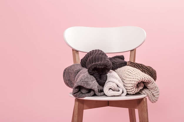 Free photo white chair with a stack of knitted sweaters on a pink wall