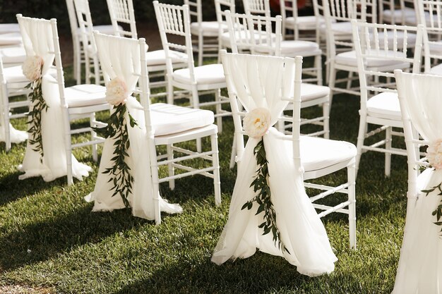 White chairs decorated with peonies and greenerty stand outside