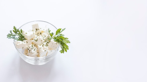 White cheese cubes with parsley in the glass bowl on white backdrop