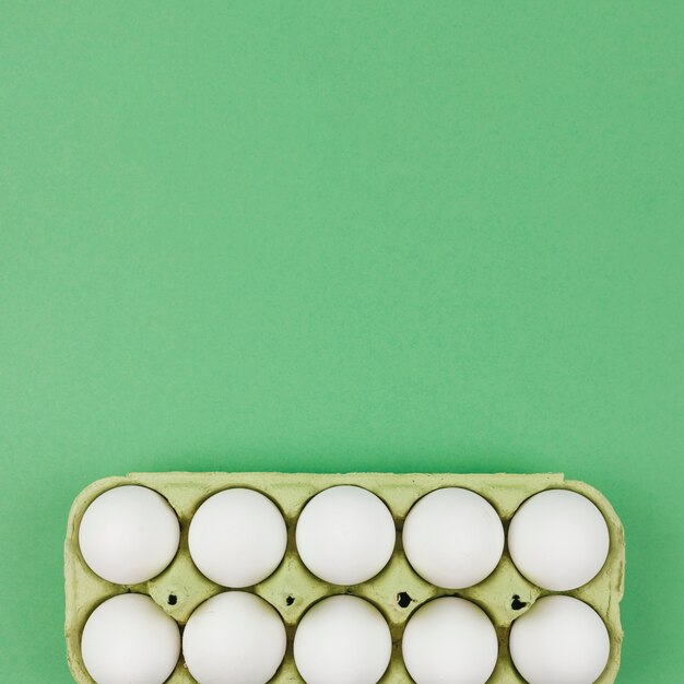 Белые куриные яйца в стойке на зеленом столе