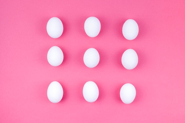 Белые куриные яйца, разбросанные на розовом столе