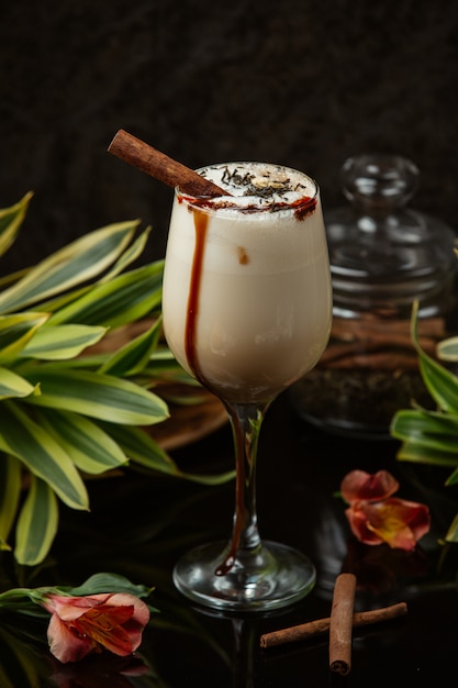 белый шоколадный кофе в стакане со взбитыми сливками и палочкой корицы