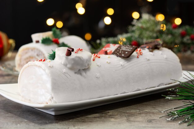 White chocolate yule log cake with christmas lights on wooden table