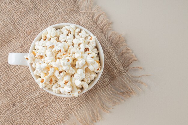 White classic popcorns in a white cup on a piece of burlap.