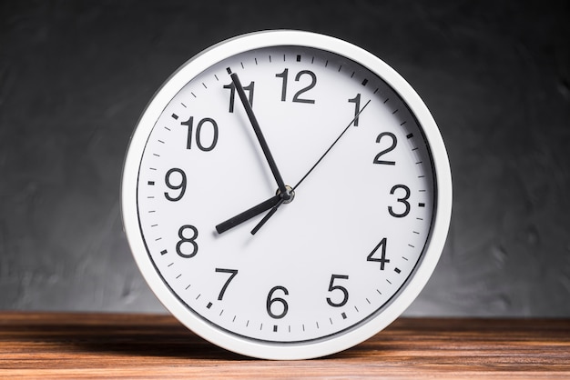 White clock on wooden desk against black background