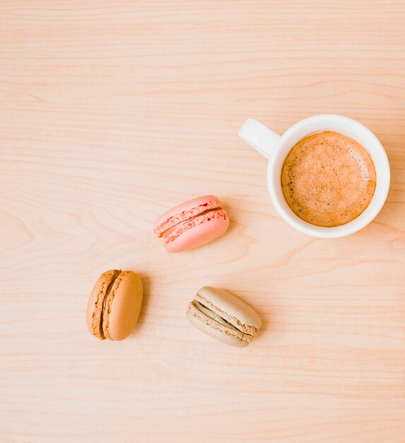 White coffee cup and macaroons on wooden textured backdrop