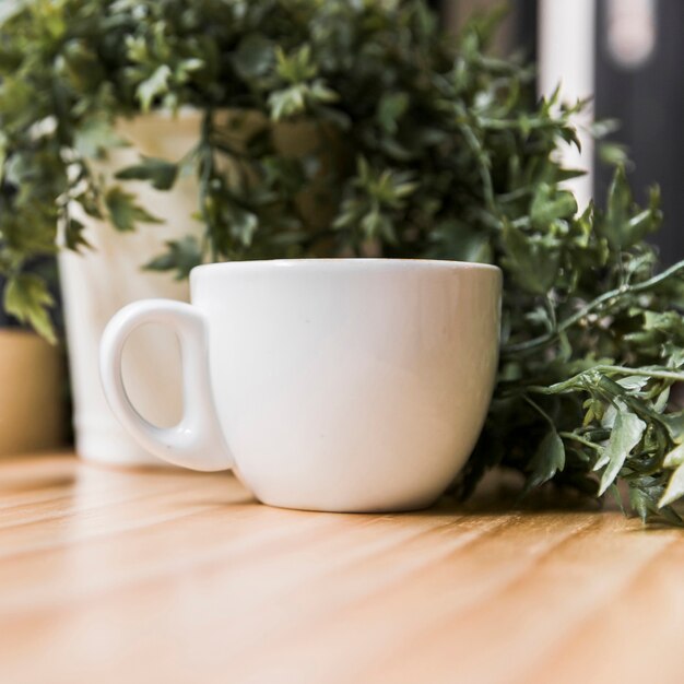 Белая чашка кофе с горшечным растением на деревянном столе