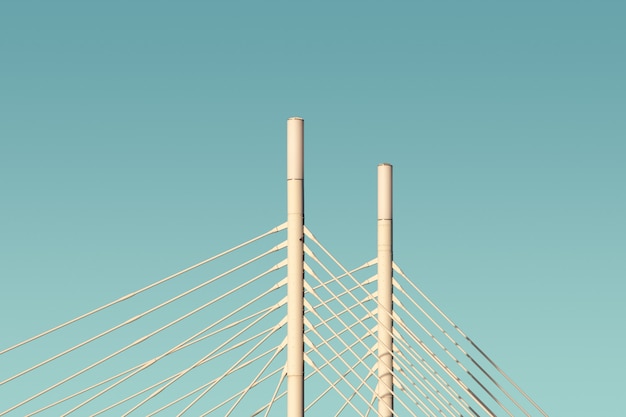 Белые колонны и кабели моста с голубым небом на заднем плане