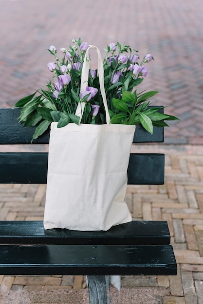 Белая хлопчатобумажная сумочка с красивыми фиолетовыми цветами эустомы в черной скамье