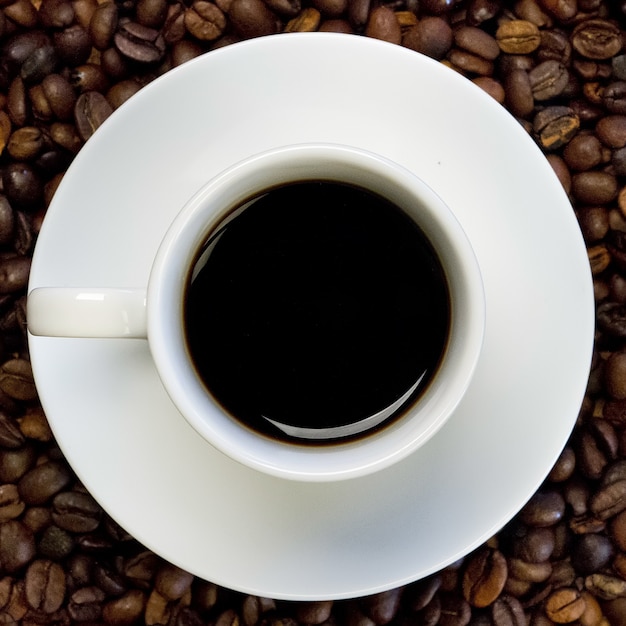 Foto gratuita una tazza bianca di caffè nero su una superficie piena di chicchi di caffè