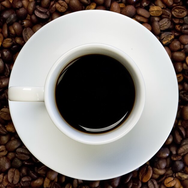 a white cup of black coffee on a surface full of coffee beans