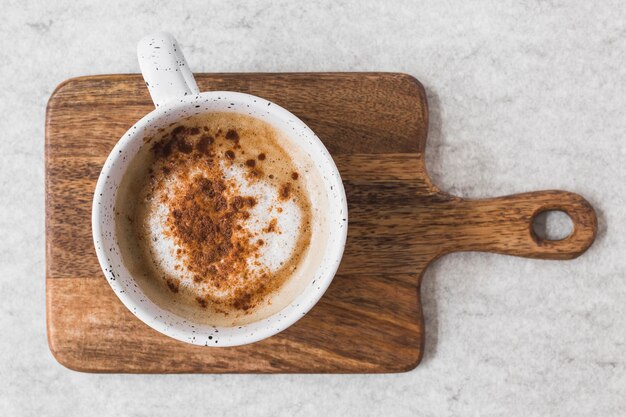 白いカップのカプチーノはチョッピングボード上に粉末チョコレートを振りかける