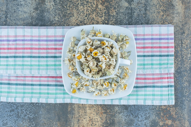 Foto gratuita tazza bianca piena di camomilla essiccata sulla tovaglia.