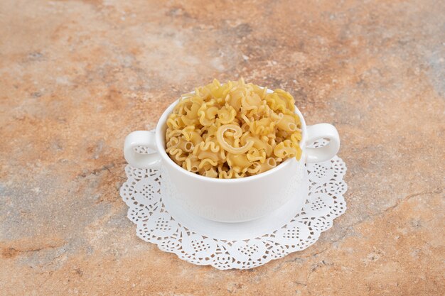 A white cup full of unprepared fresh macaroni on marble background. High quality photo