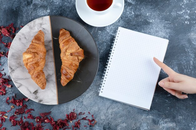 A white cup of hot tea with an empty notebook placed on a marble table. 