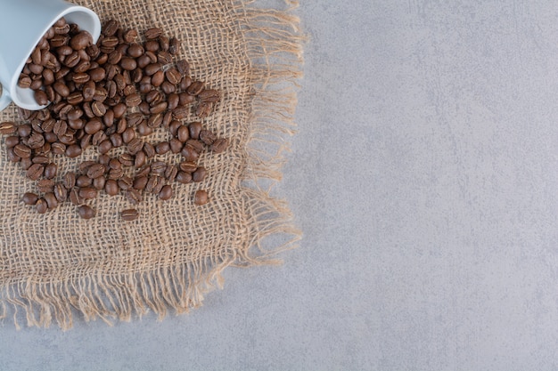 A white cup of roasted coffee beans on marble background.