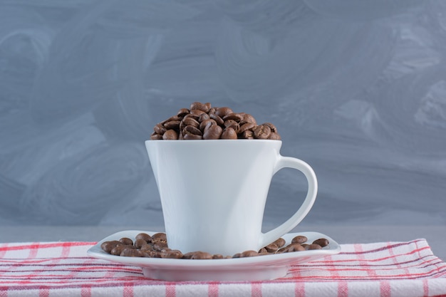 Белая чашка жареных кофейных зерен на полосатой скатерти.