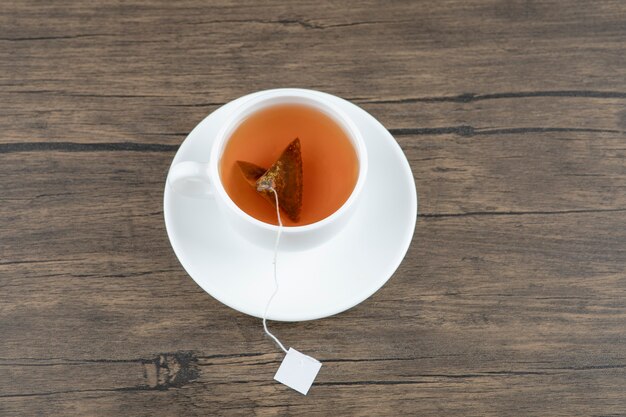 A white cup of tasty hot tea with teabag on a wooden table.