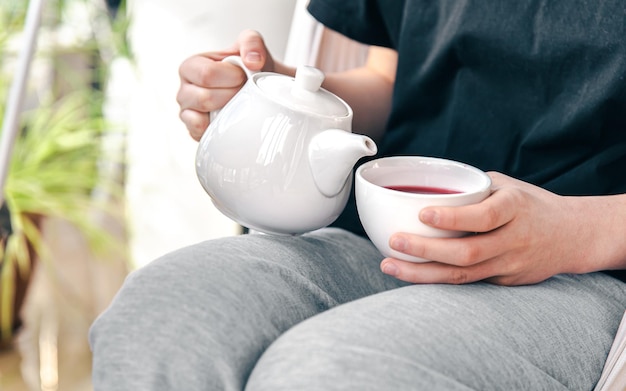 A white cup of tea and a teapot in a womans hands