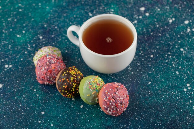 A white cup of tea with small delicious doughnuts .