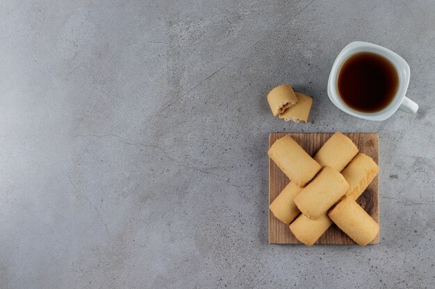 A white cup of tea with sweet fresh cookies in a wooden board on a stone.