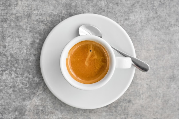 White cup with fragrant strong espresso coffee with thick foam in a traditional Greek coffee shop Top view of coffee with saucer on gray marble table idea for background or poster