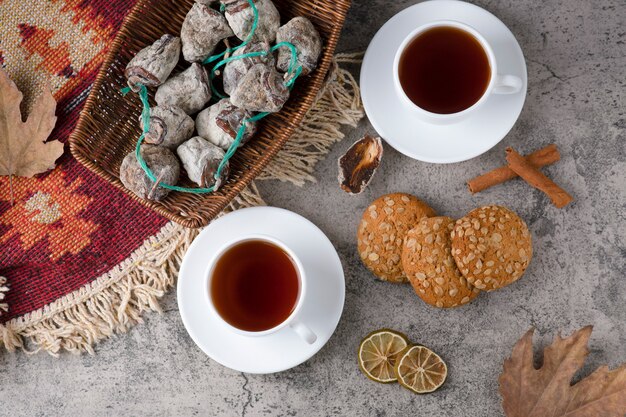 White cups of hot tea with dried fruits and oatmeal cookies on a stone table. 
