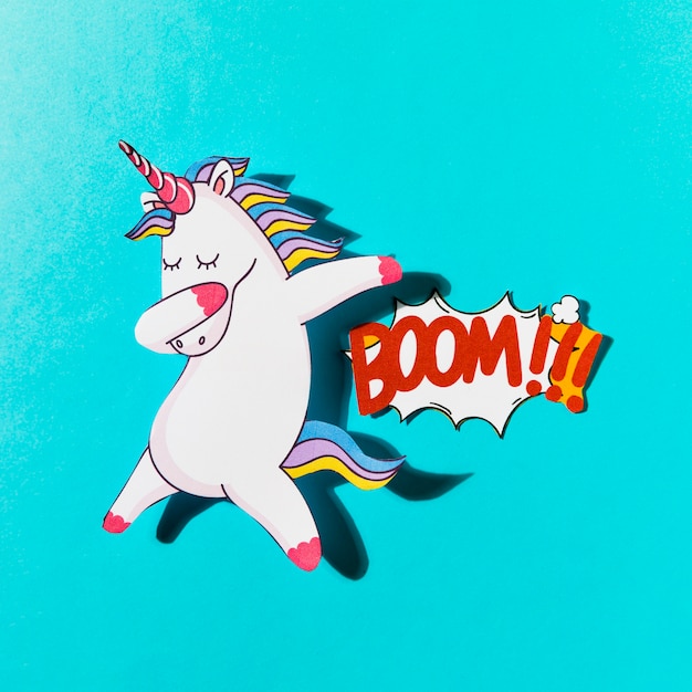 White dabbing unicorn with boom comic text on blue backdrop