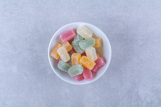 A white deep plate full of colorful bean candies on gray background. High quality photo