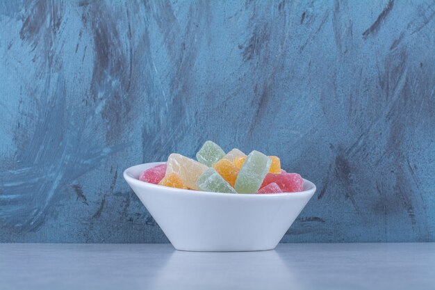 A white deep plate full of colorful bean candies on gray table. 